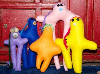 Five brightly colored handmade dolls arranged against a red cabinet